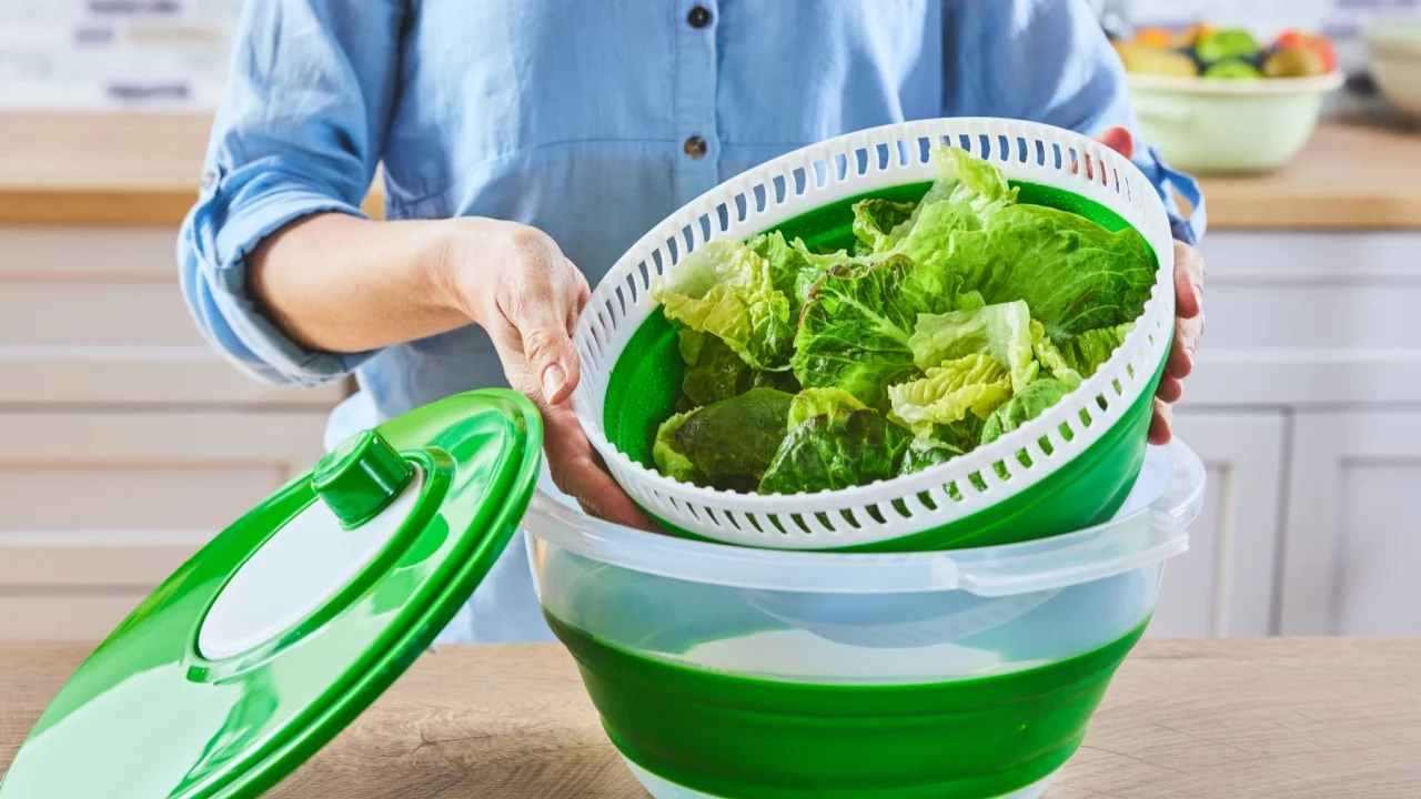 Anonymous woman in blue shirt removing bowl with fresh lettuce from spinner while cooking healthy food in kitchen at home