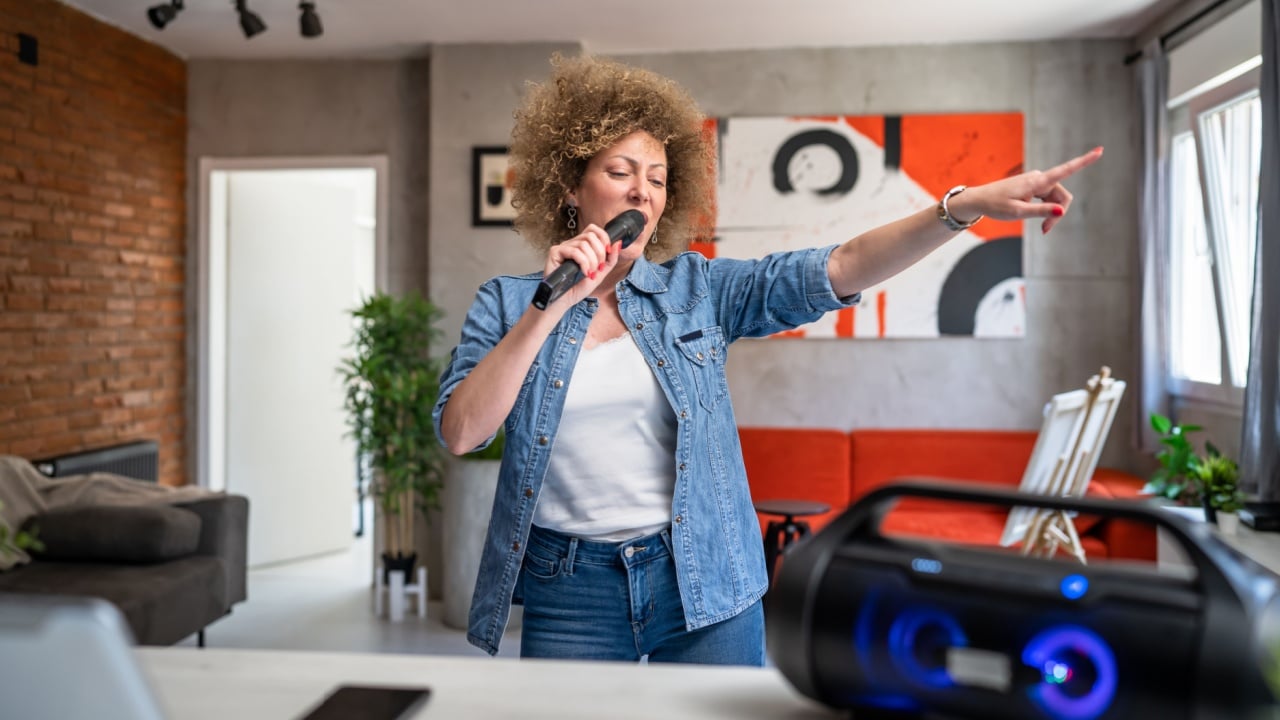 One woman adult caucasian female with curly hair having a good time at home in room singing and dancing hold microphone having fun with karaoke and music joyful rhythm alone real people copy space