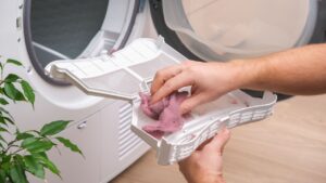 A man holds a dirty dryer filter. A man collects lint, hair, wool from the filter of a drying machine. Red lint on the dryer filter. Dirty filter dryer.