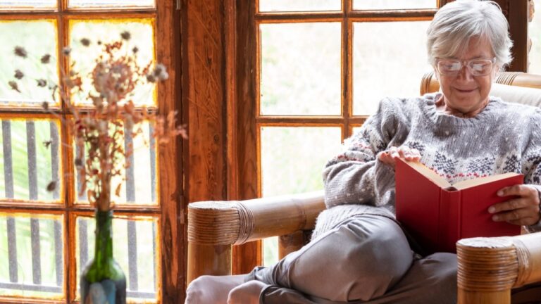 Attractive relaxed senior woman sitting at home in an armchair reading a book. Elderly smiling caucasian woman enjoying reading pleasure in retirement
