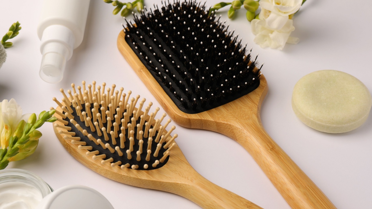 Wooden hairbrushes, different cosmetic products and beautiful flowers on white background