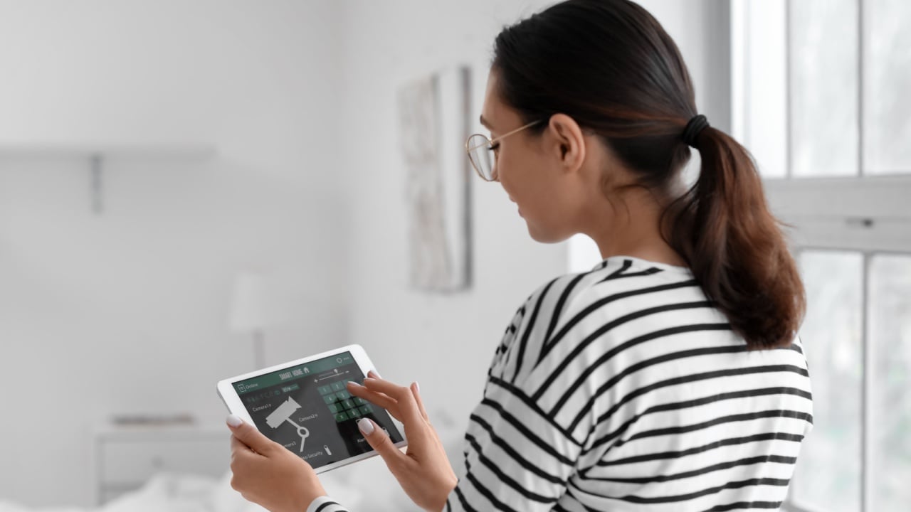 Young woman using smart home security system control panel in bedroom