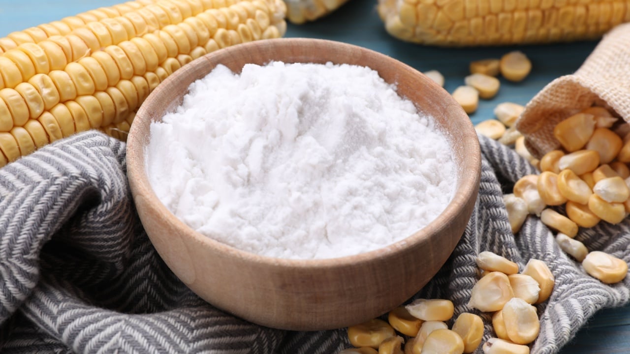 Bowl with corn starch, ripe cobs and kernels on table.