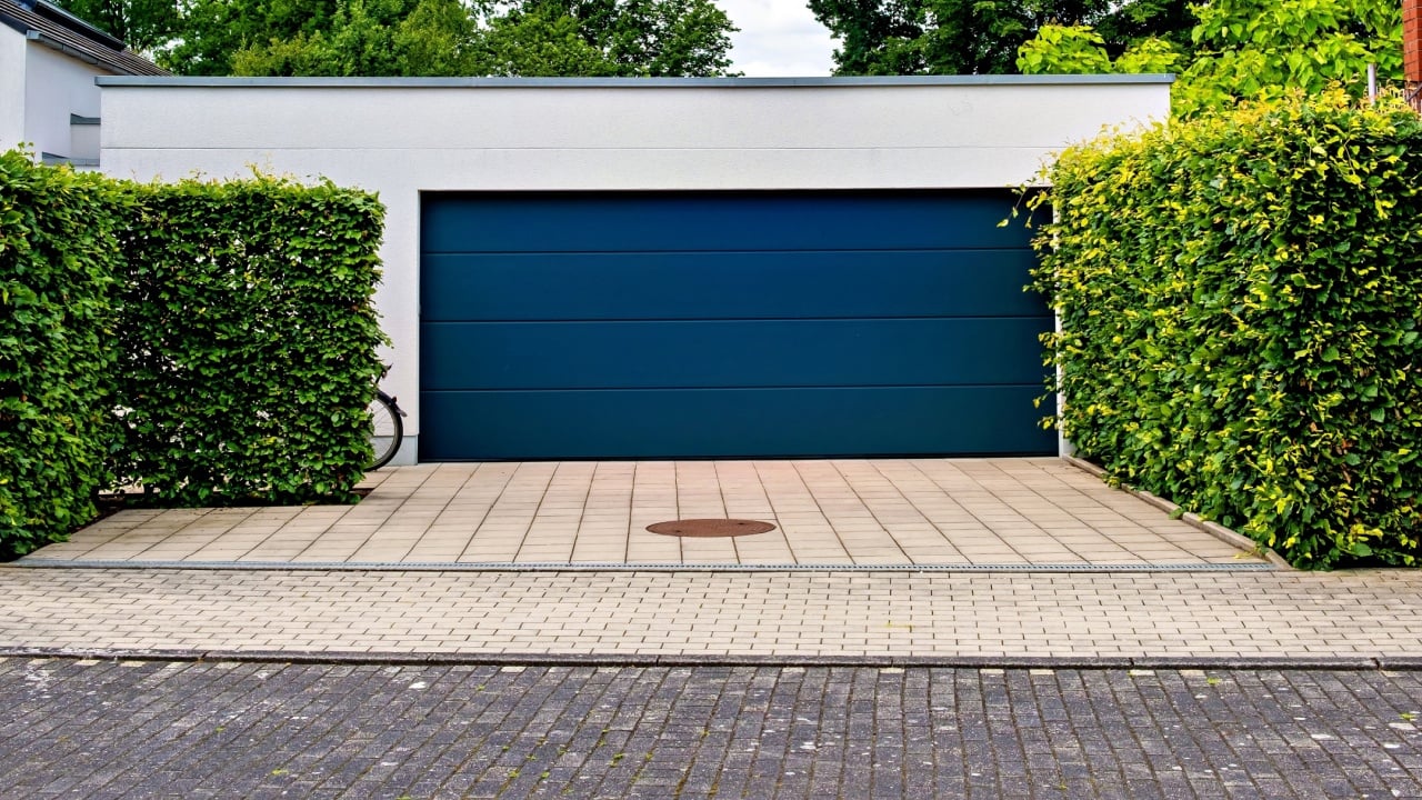 House with blue garage door in front of hedged driveway in Germany.