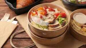 Tasty food in containers with knife and fork on wooden table.