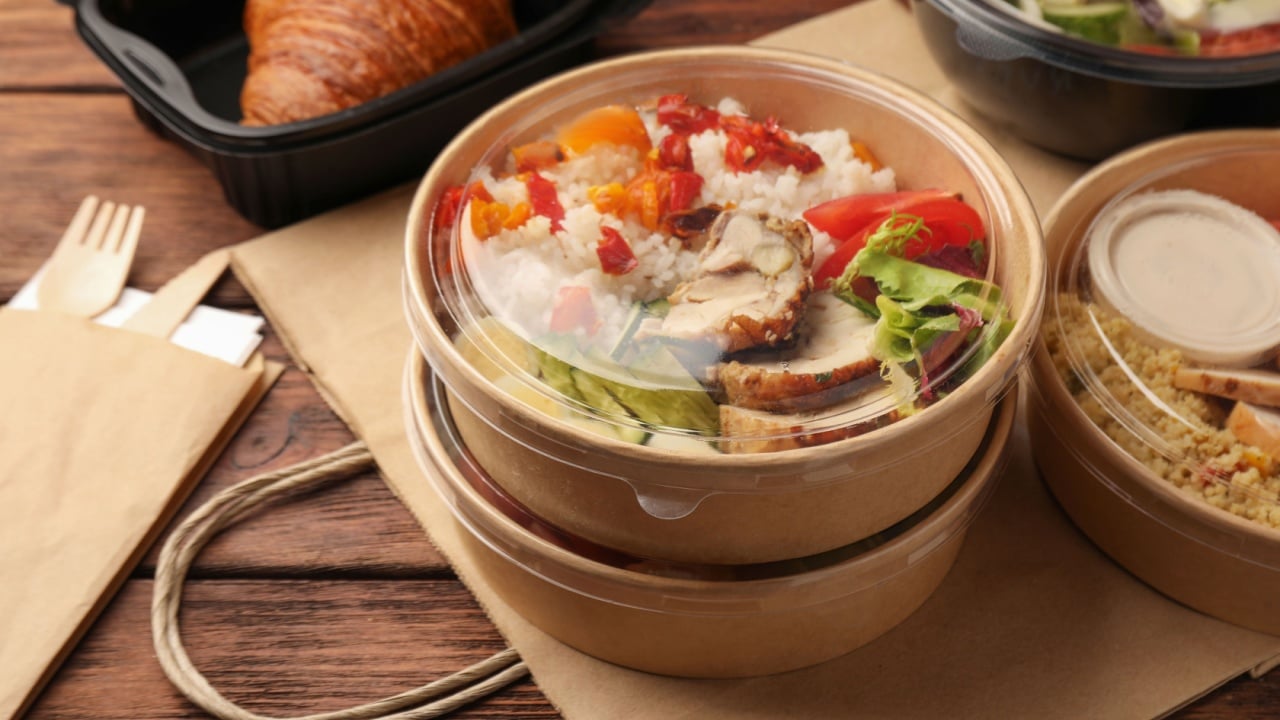 Tasty food in containers with knife and fork on wooden table.