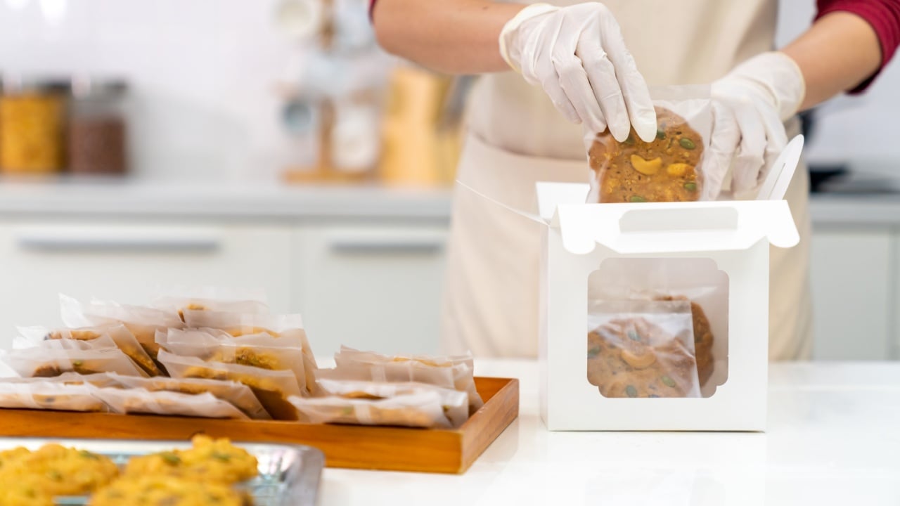 Asian woman hand pastry chef bakery shop owner preparing catering customer order cookies in delivery snack box on kitchen counter. Small business food and drink occupation entrepreneur concept.