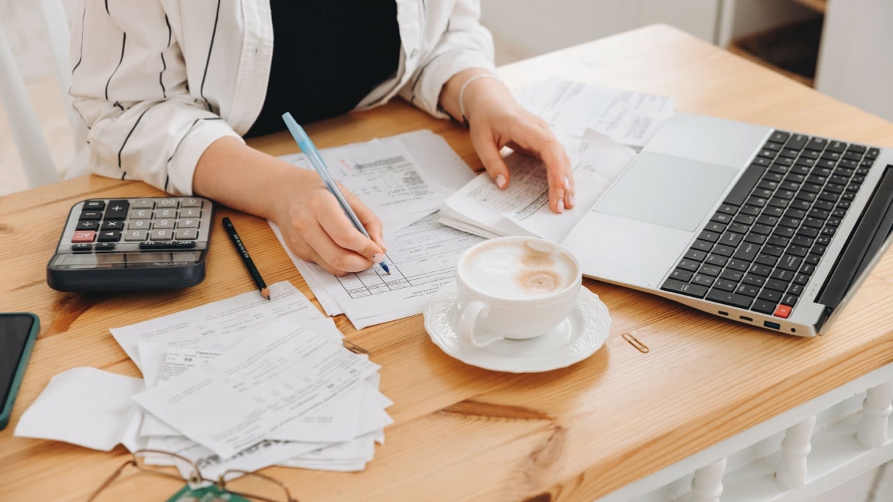 Close-up hands of unrecognizable woman work at home in the kitchen with financial papers, counting on a calculator, paying bills, planning a budget to find a way to save money. Independent accounting