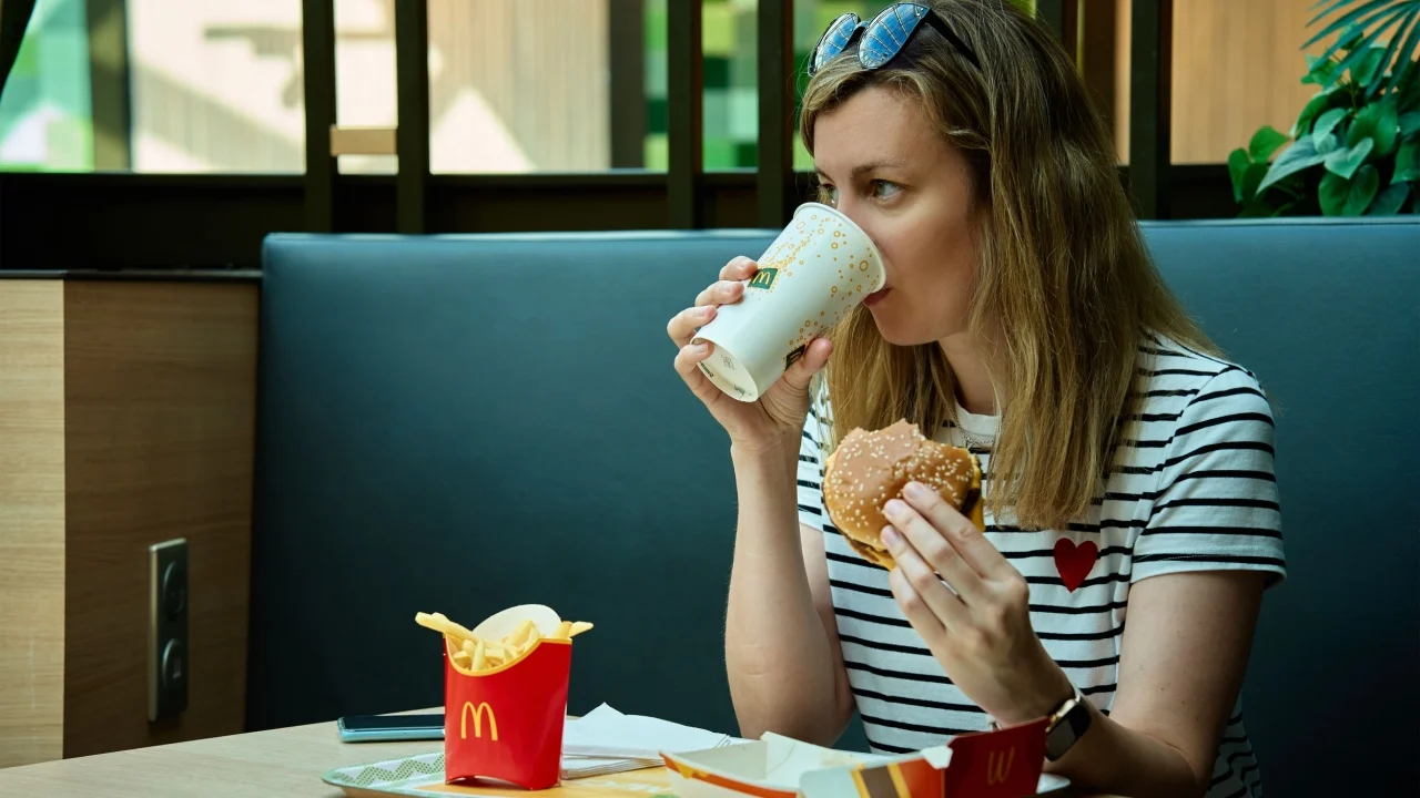 Woman has breakfast in Mcdonald's restaurant. Female eating eating hamburger and french fries in Mccafe. Fast food nutrition. Wroclaw, Poland - July 2, 2023