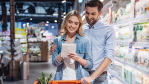 Beautiful couple is reading lists of goods and smiling while doing shopping at the supermarket