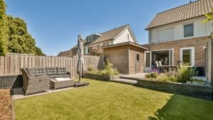 a backyard area with lawn, couch and fenced in the back yard on a clear blue sky day.