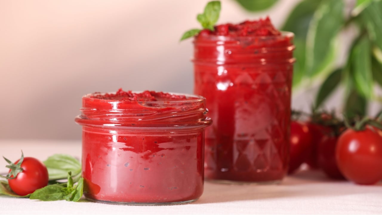Jars of tasty tomato paste and ingredients on white table,