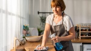 Caucasian senior elderly woman wearing apron, cleaning kitchen at home. Attractive mature old housekeeper cleaner feel tired and upset while wiping dining table for housekeeping housework or chores.