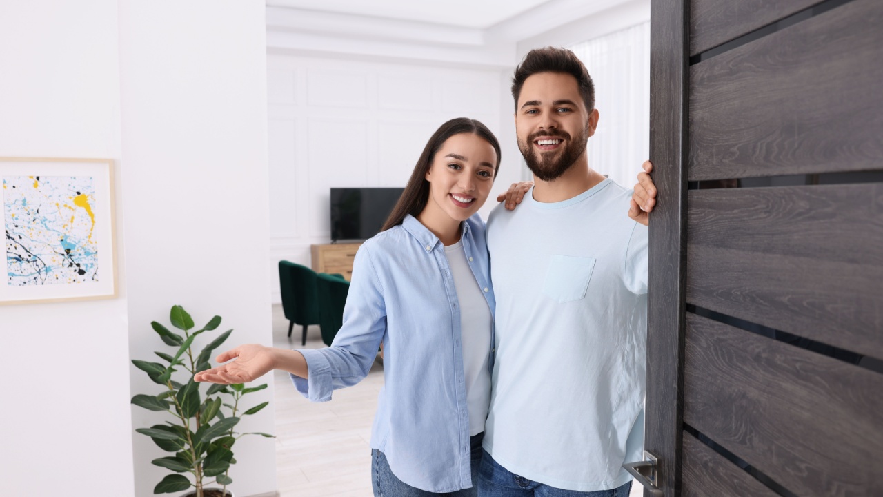 Happy couple welcoming near door. Invitation to come indoors