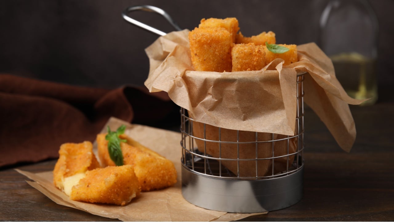 Metal basket with tasty fried mozzarella sticks on wooden table, closeup