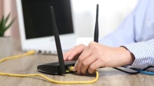 Woman inserting ethernet cable into Wi-Fi router at wooden table indoors.