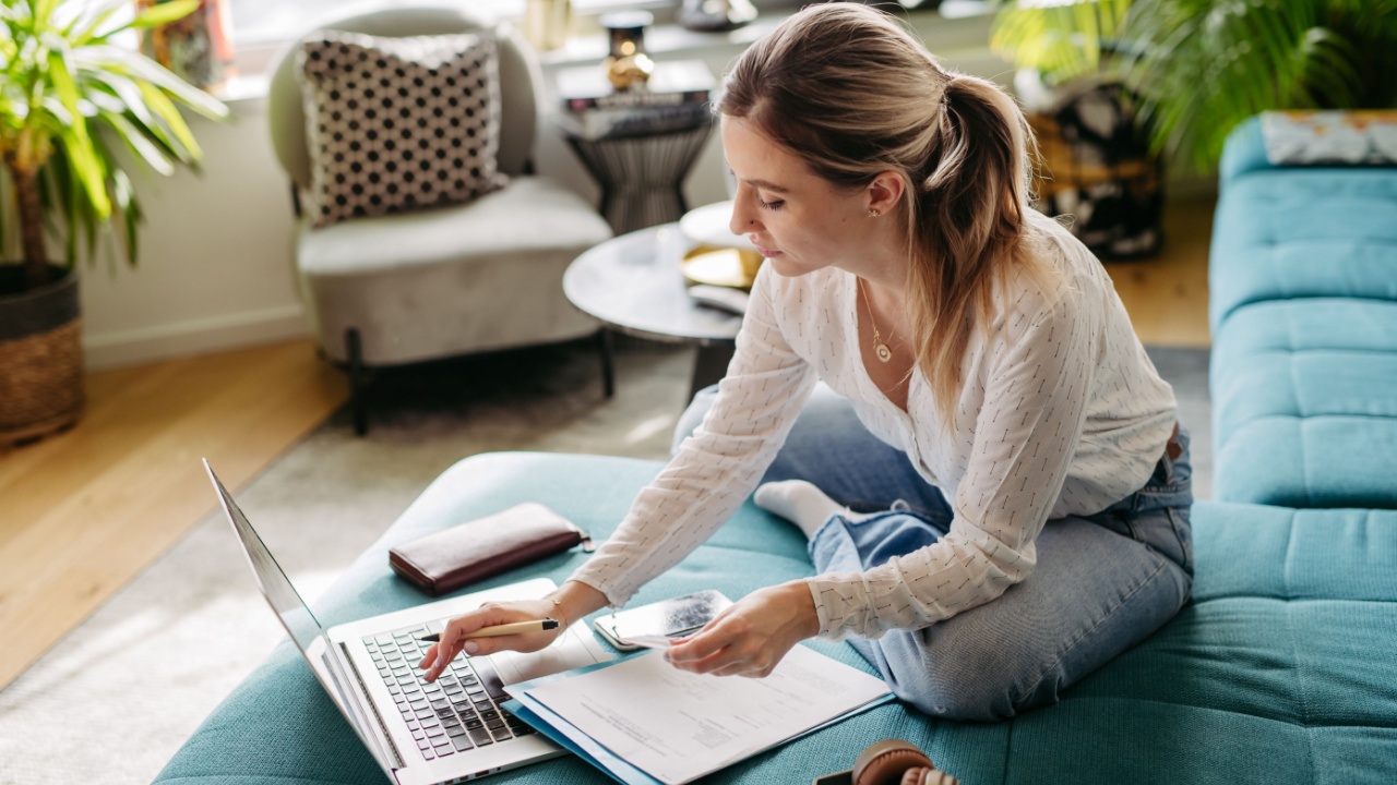 Woman paying bills online, sitting in living room, working on notebook. Online banking, internetbanking at home throught website, app.