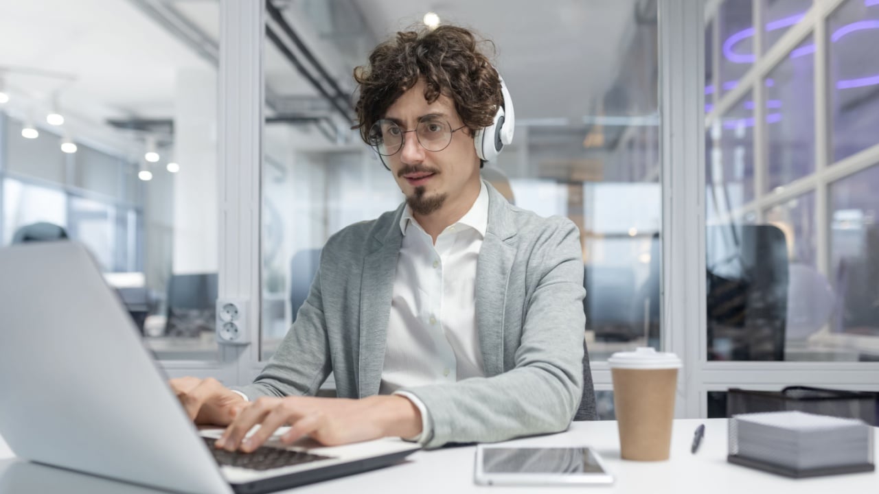 Focused adult male office worker displaying professionalism while using laptop. Emotionally invested and experienced in business tasks.