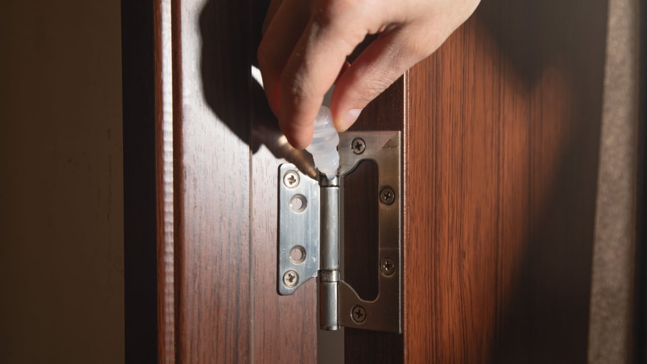 Caucasian man lubricates door hinges with oil.