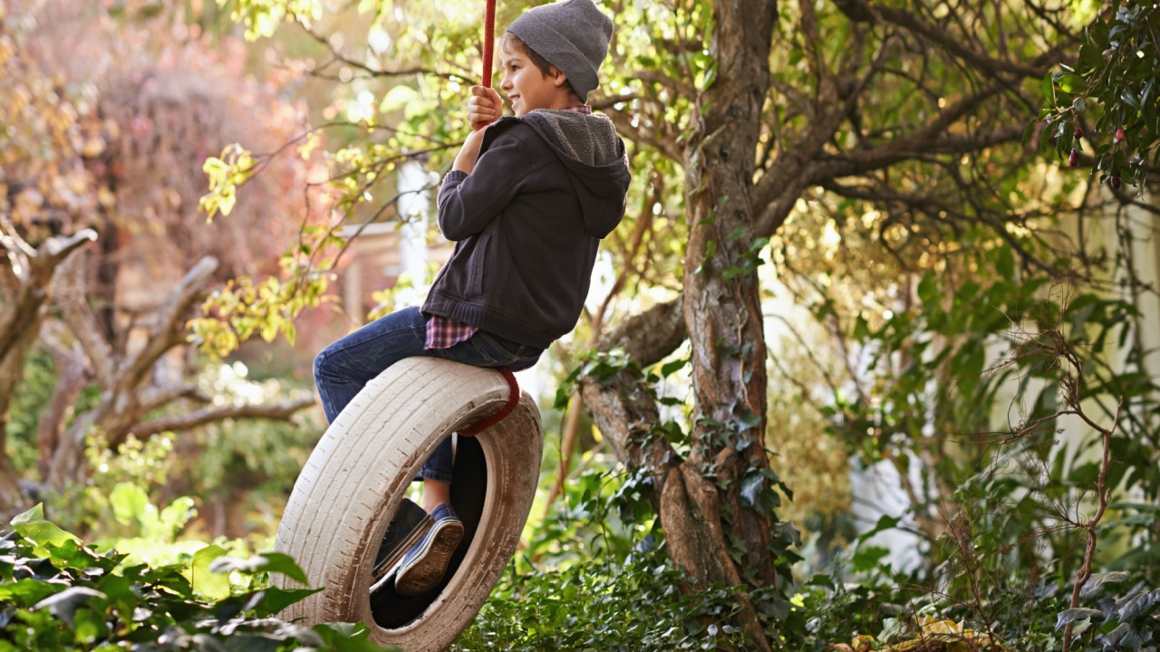 Boy, tyre swing and playing in garden with happiness, recreation and countryside vacation in summer. Child, smile and diy adventure playground in backyard of home with sunshine and trees in nature