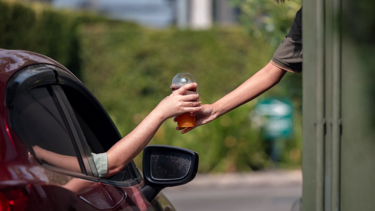 Hand Man in car receiving coffee in drive thru fast food restaurant. Staff serving takeaway order for driver in delivery window.