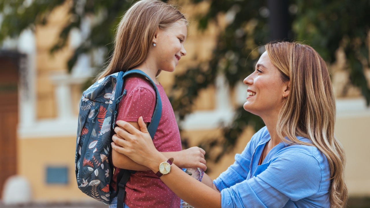 Mother accompanies the child to school. Mom supports and motivates the student.caring mother gently kisses her daughter on the forehead. Positive little girl fun going to primary school.Back to school