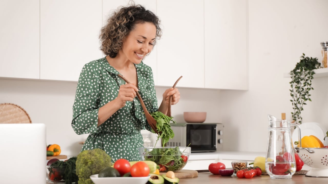 Mature woman stirring vegetable salad in kitchen
