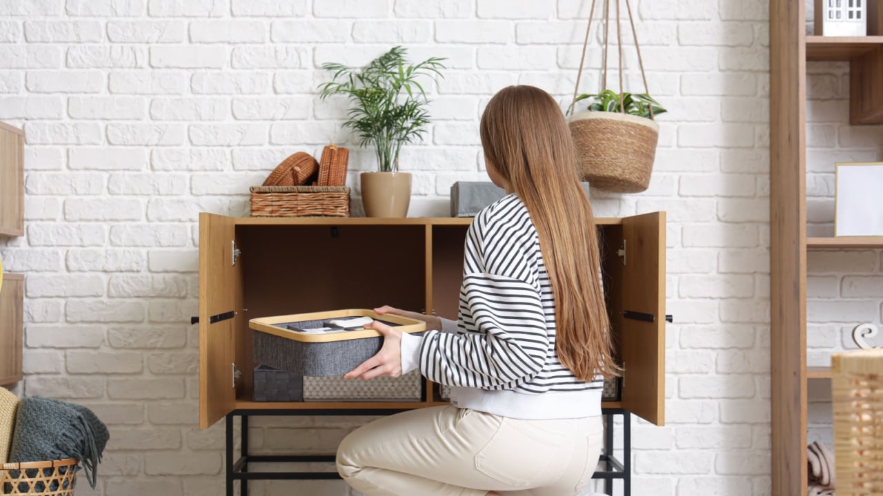 Young woman putting organizers with clothes in cabinet at home