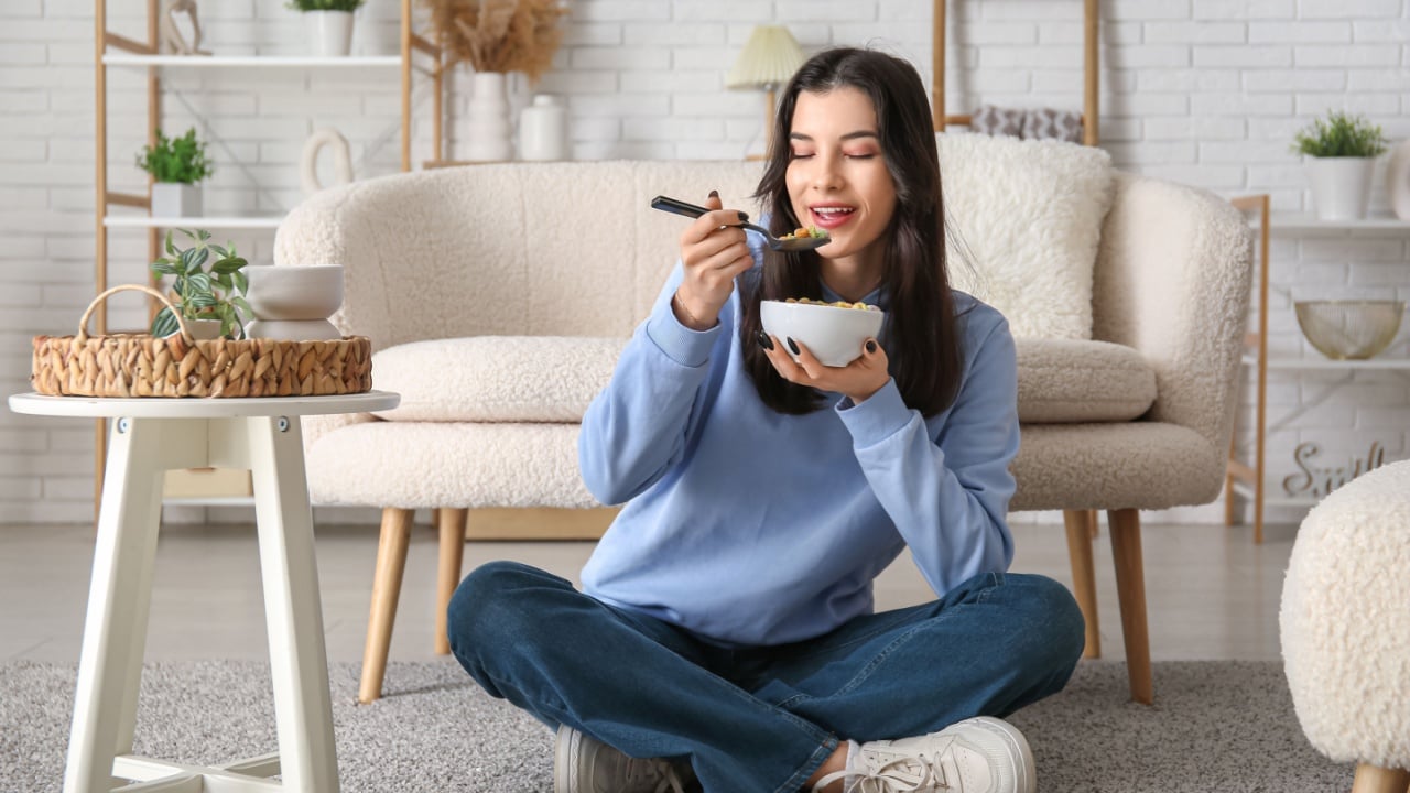 Young woman eating tasty cereal rings at home