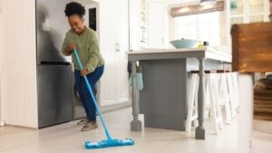 Happy senior african american woman cleaning floor with mop at home. Domestic life, retirement, cleaning and lifestyle, unaltered.
