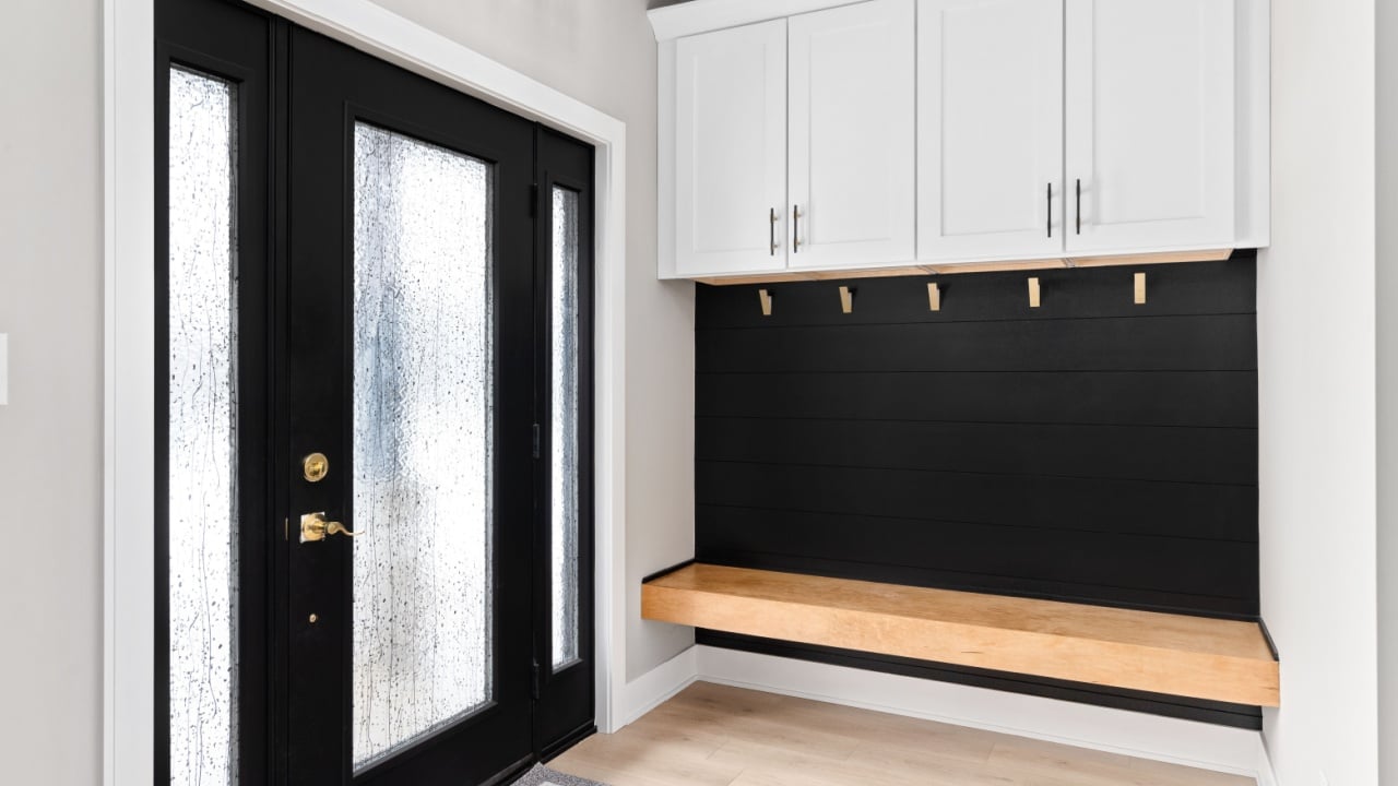 A modern farmhouse entryway with bench seating, black shiplap, white cabinets, gold coat hooks, and a black and gold light fixture,