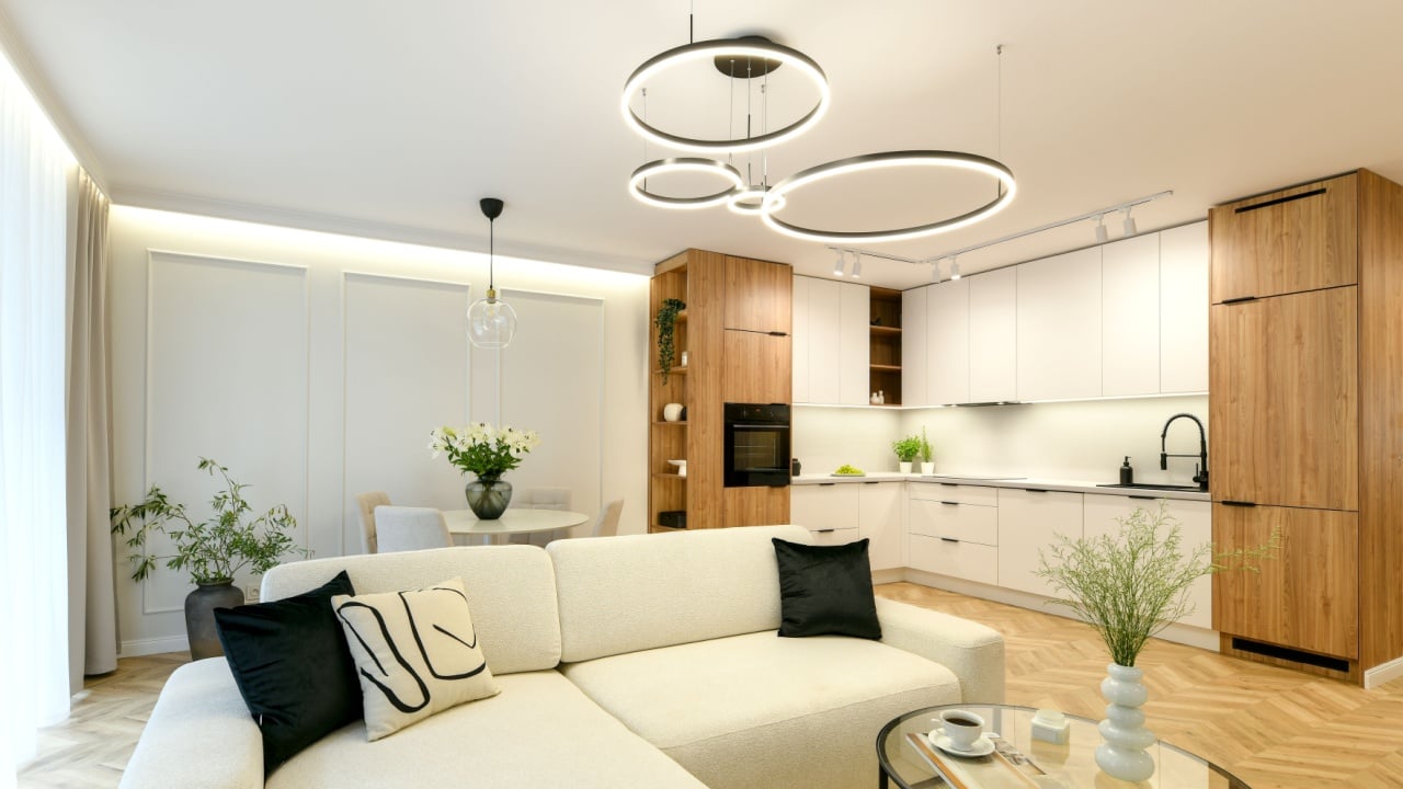 Photo of elegant spacious living room in modern classic style with open kitchen, white big sofa, herringbone floor and circle led lamp