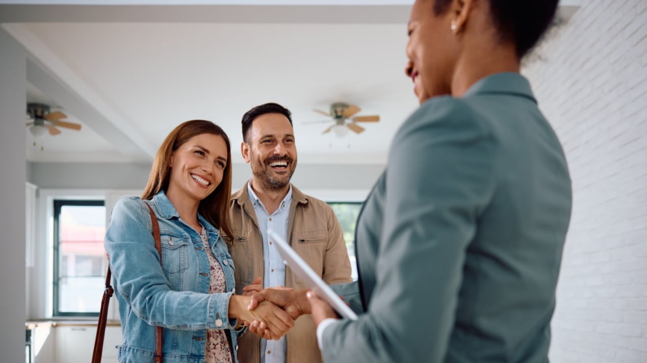 Happy woman shaking hands with real estate agent while buy new home with her husband.