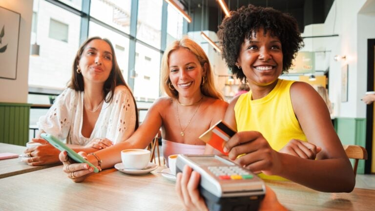 A cheerful young African American woman is settling her bill with a contactless creditcard at a restaurant. She smiles as she hands over her credit card to complete the payment with the cashier.