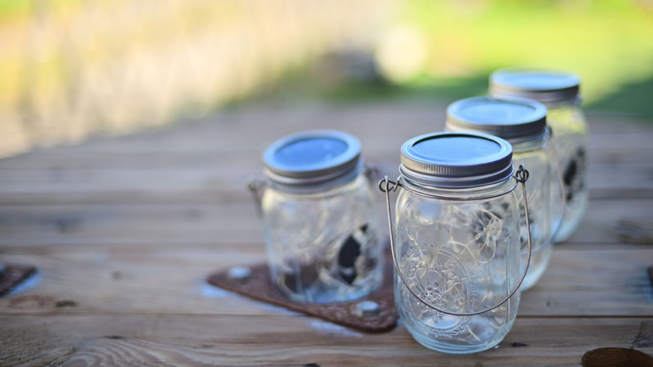 Early morning dim light reveals several unlit Ball Mason Jar solar lights on a wooden table, showcasing their design and outdoor ambiance.