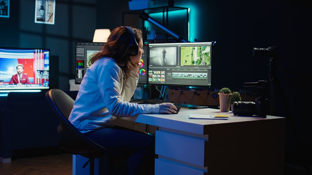 Videographer working on film montage, editing color grading and listening music. Post production studio worker manipulating raw footage, doing adjustments, wearing headphones, camera B
