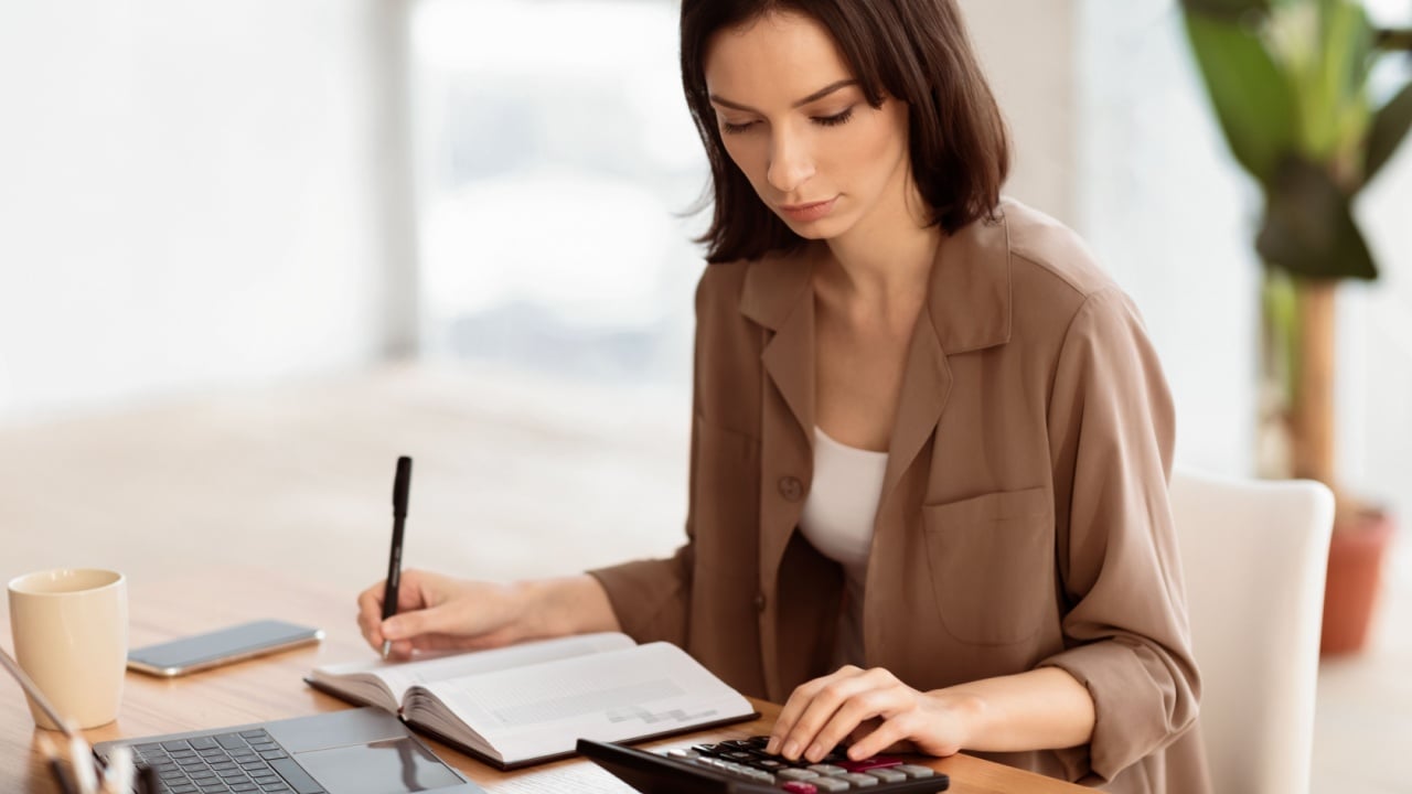 Budget Planning. Focused young woman using calculator, counting income and expenses and writing