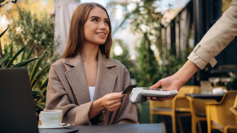 Positive, cheerful facial expression. Woman is paying for food in cafe by using credit card. Conception of wireless money transfer.