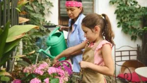 A mother and daughter enjoy a sunny day gardening, nurturing pink flowers in a vibrant garden. Their teamwork and focus highlight a shared love for nature, family bonding, and care.