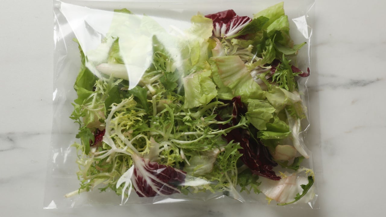 Pack of fresh salad mix on white marble table, top view