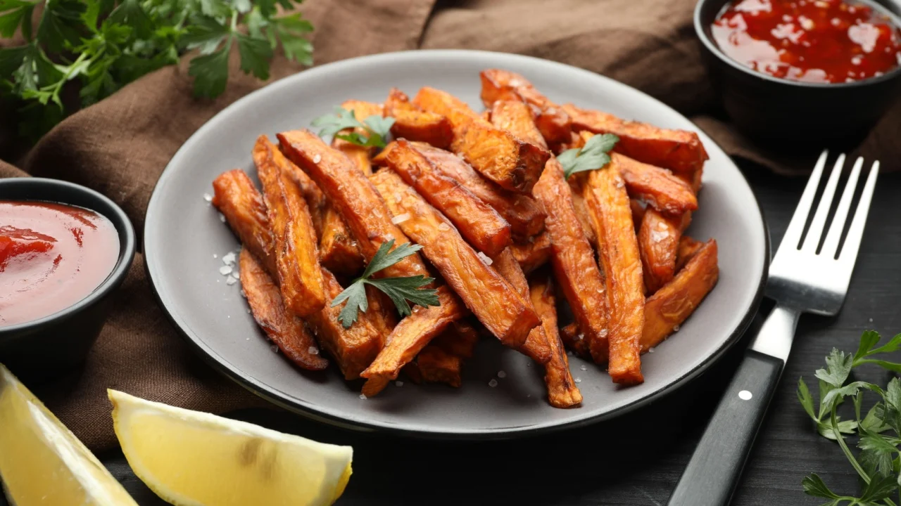 Delicious sweet potato fries with spices and sauces on black wooden table.