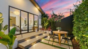 Modern backyard patio with cozy seating and ambient lighting at sunset, featuring lush greenery and a stylish deck.