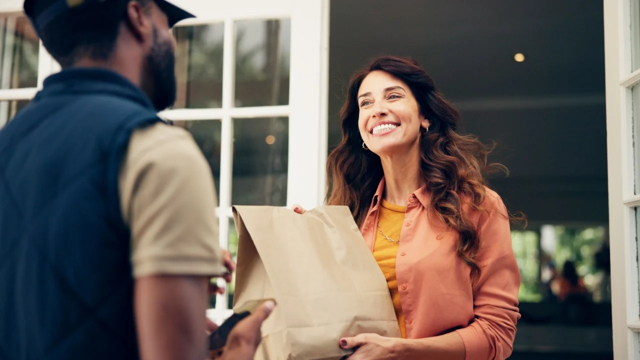 Delivery man, woman or courier with phone for package by front door for online shopping order or fast food distribution. Logistics, customer or male driver with paper bag for ecommerce or safe parcel