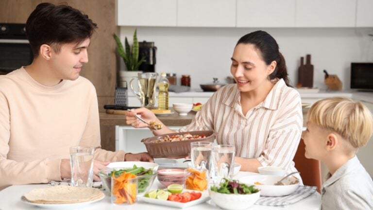 Young woman putting Fajita on her husband's plate at family dinner in kitchen