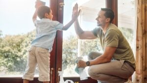 Cleaning, door and high five of father with son in living room of home together for weekend chores. Motivation, success or teamwork of man parent and boy child in apartment with rag and spray bottle