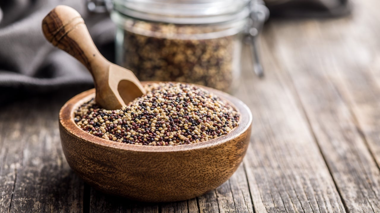 Mixed uncooked quinoa seeds in bowl on a wooden table.