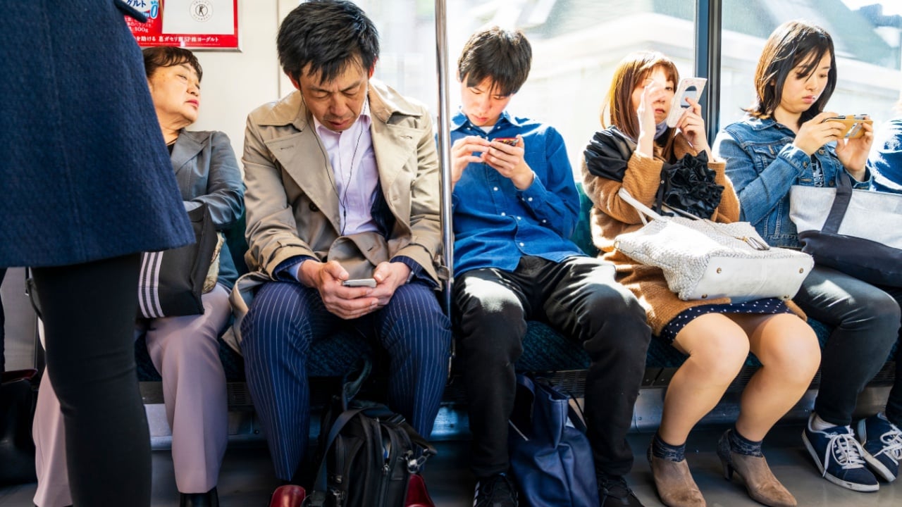 Shinjuku, Tokyo, Japan. April 15 2019. Interior of Japanese railway train with four Japanese commuters on a train sitting in a row against carriage window all using their mobile phones.