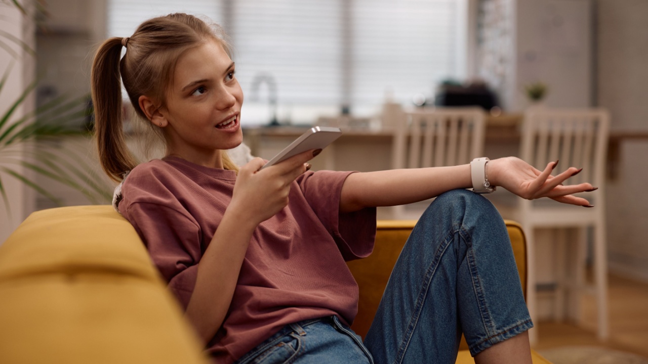 Teenage girl sending voice message over her smart phone while relaxing on the sofa at home.