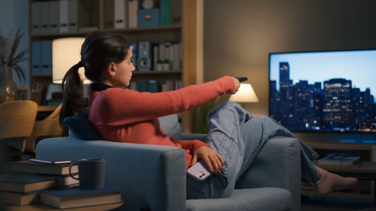Teenager relaxing on the armchair at home, she is watching TV and holding the remote control