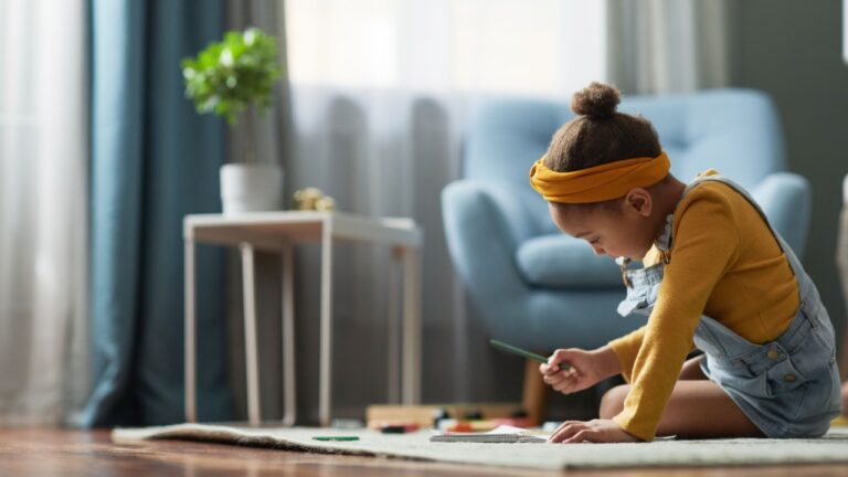 Side view portrait of cute African-American girl drawing while sitting on floor in cozy home interior, copy space